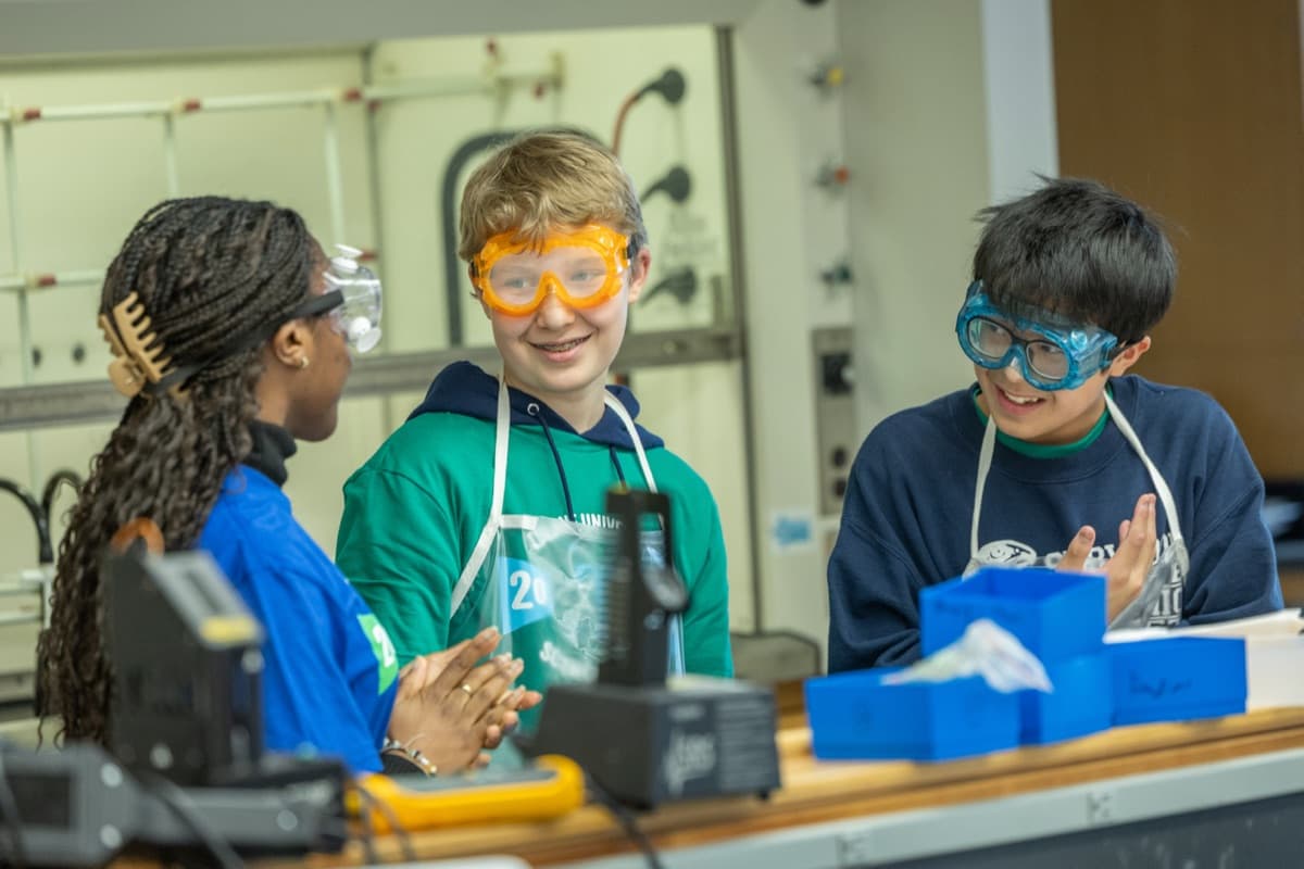 Three students in safety goggles laughing at a lab bench during the 2026 Tulane Science Olympiad Invitational